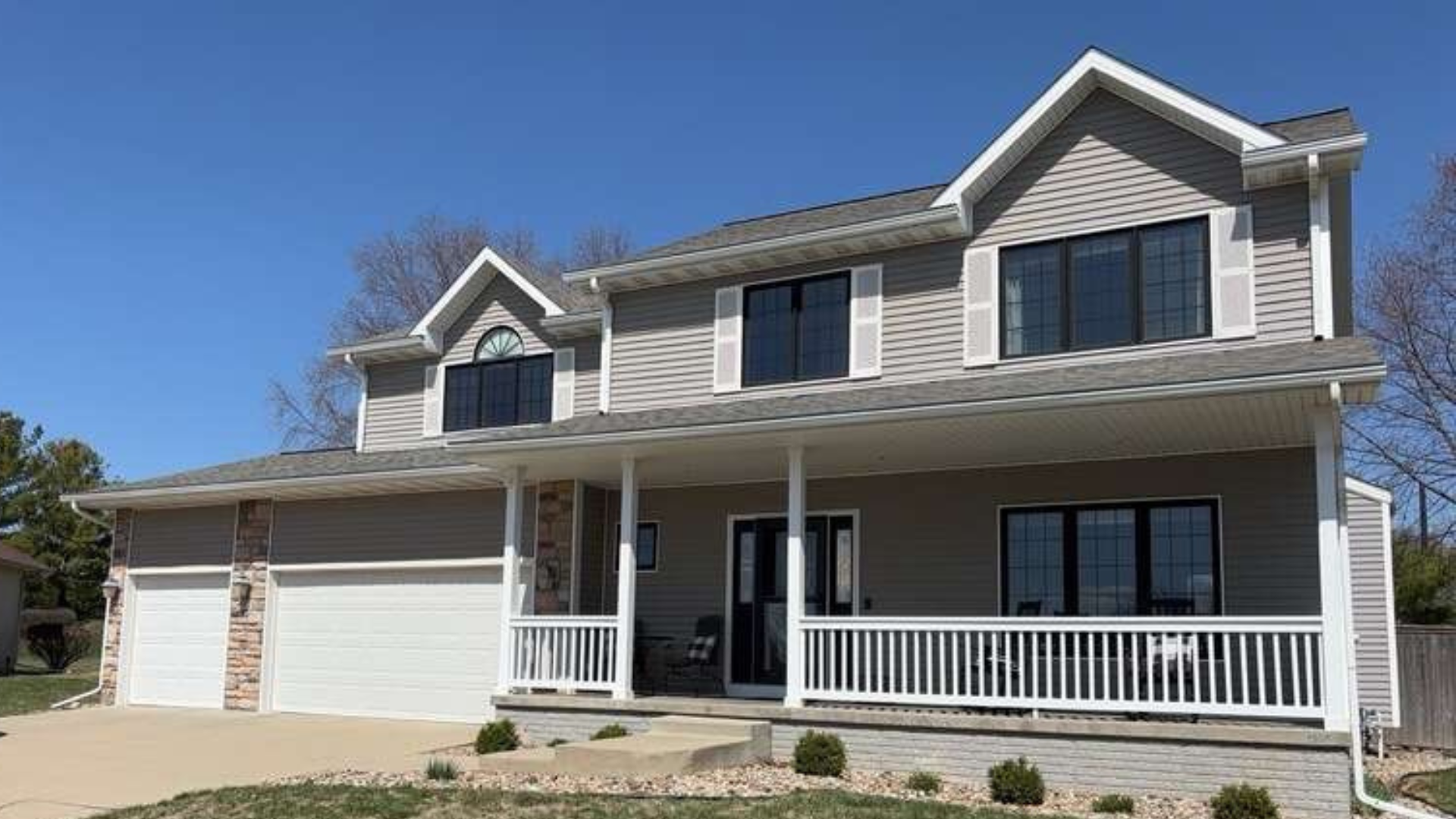 A two-story house with gray siding and black trim before a full window replacement in Johnston, Iowa.